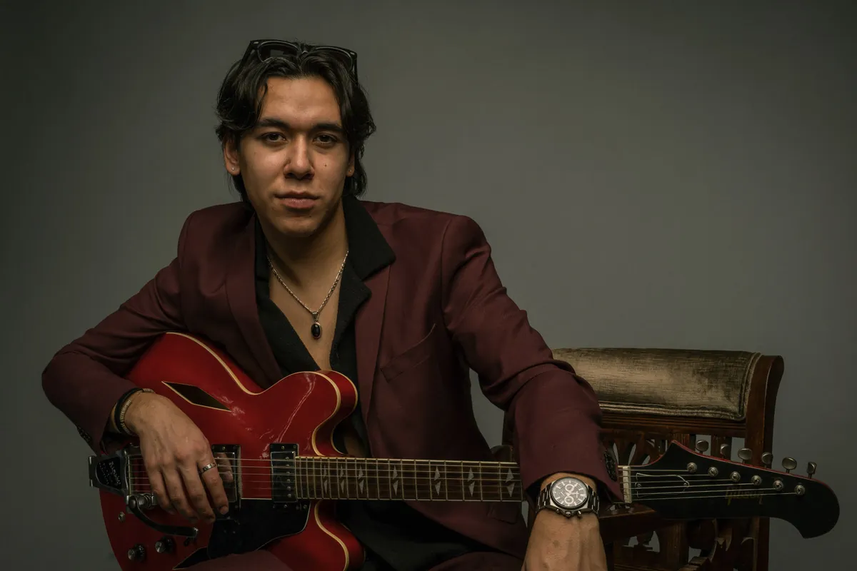 Zeegwon Shilling in a burgundy suit with his red Gibson guitar