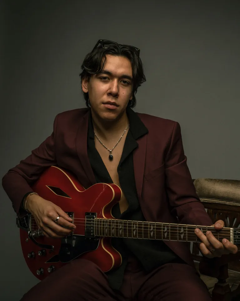 Zeegwon Shilling seated with a red Gibson guitar, looking at the camera