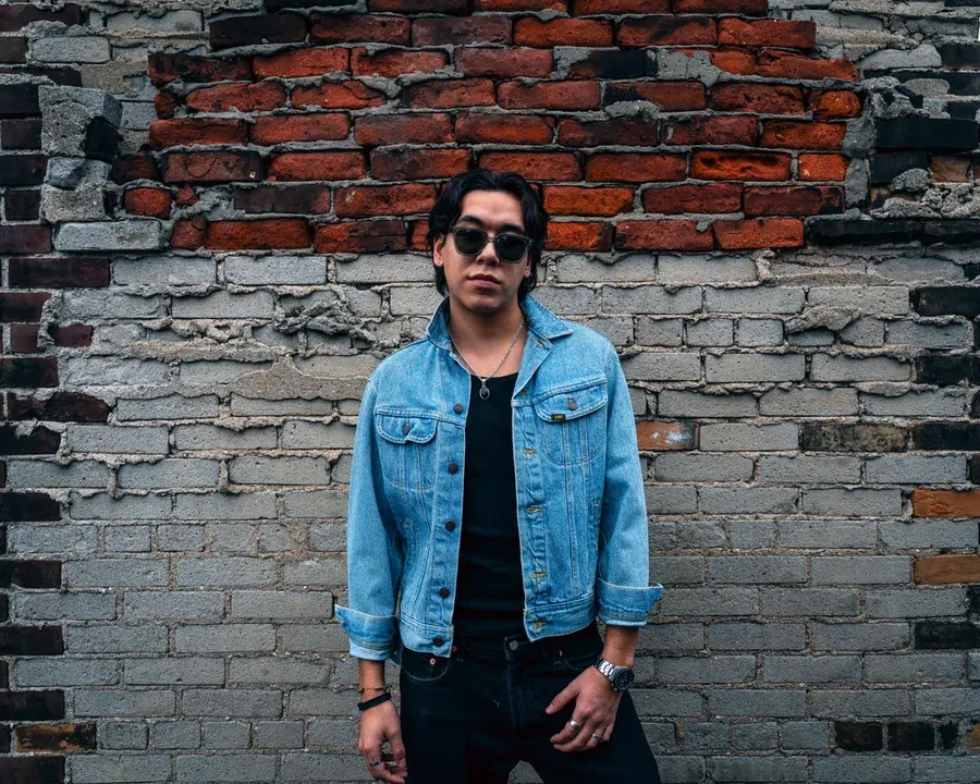 Zeegwon Shilling in a denim jacket against a brick wall in Toronto